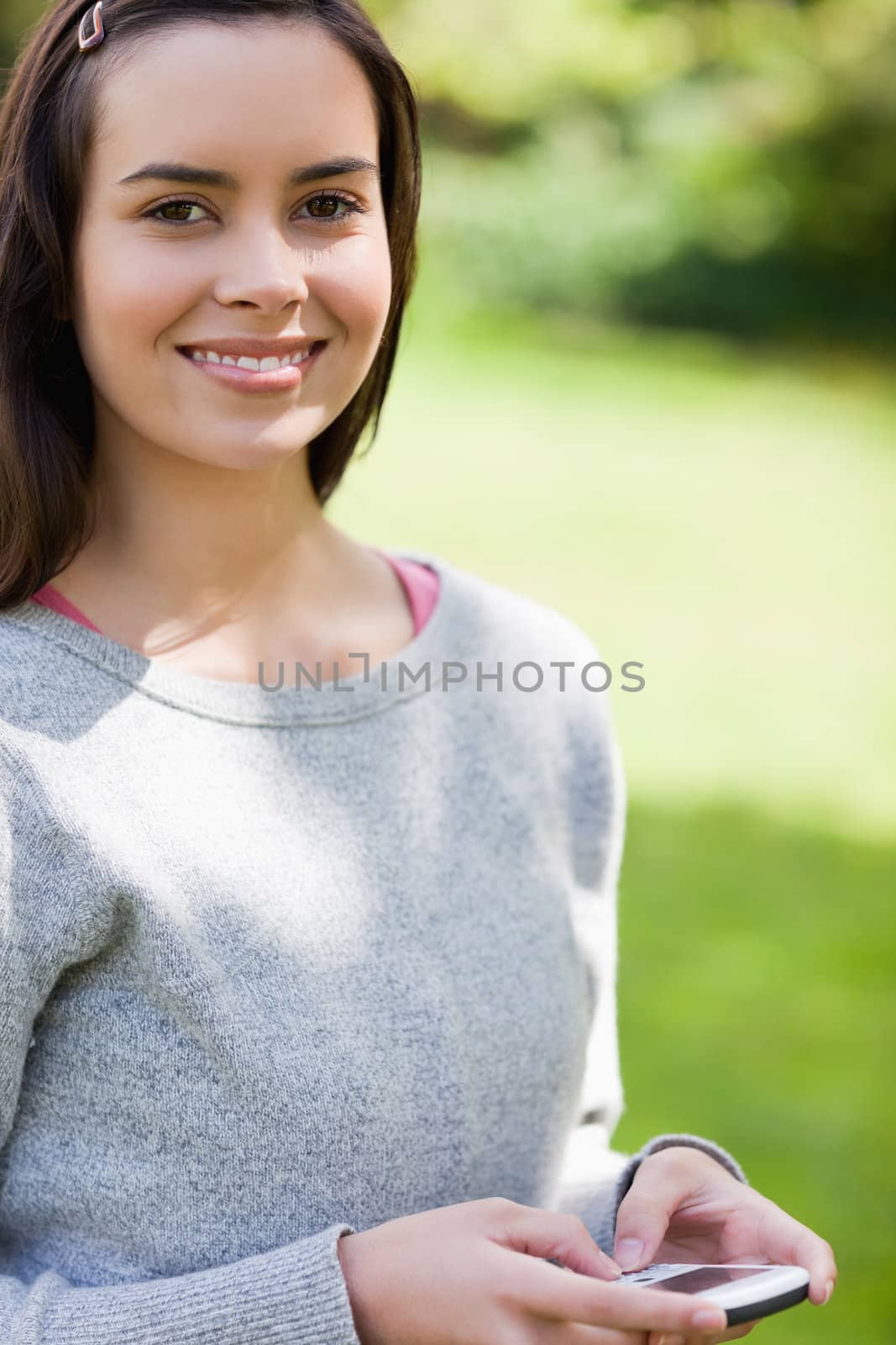 Smiling young woman using her cellphone while standing in a park by Wavebreakmedia