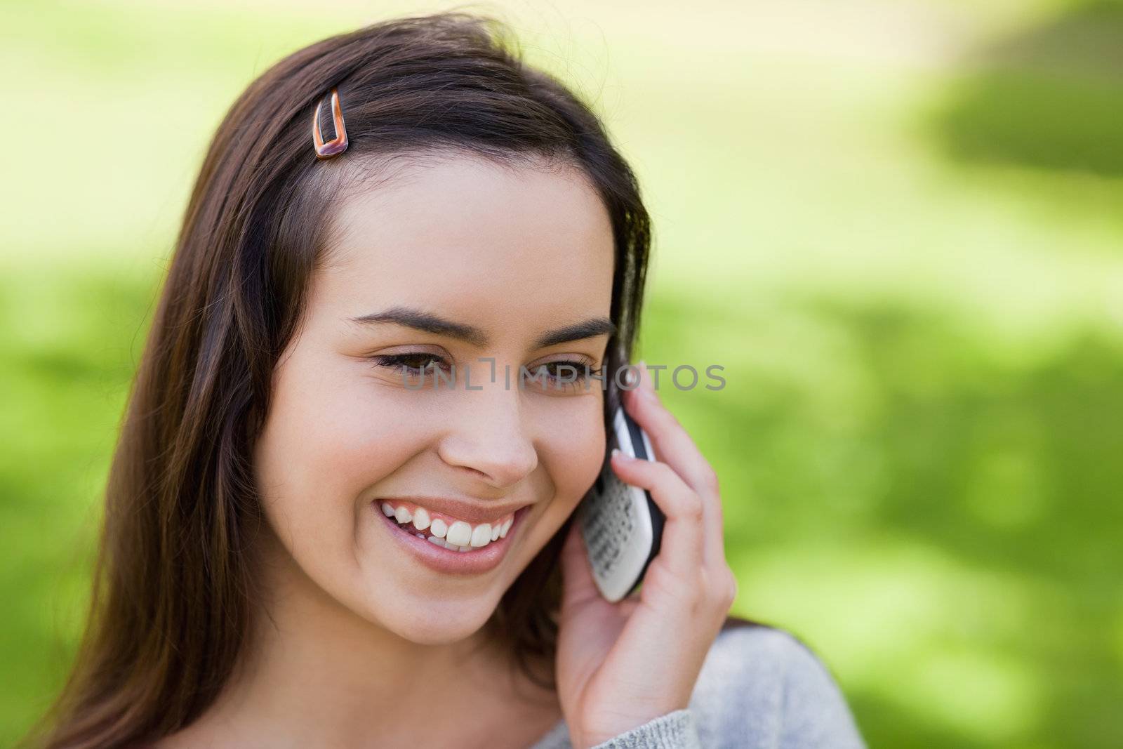 Smiling young woman using her mobile phone while standing in a parkland