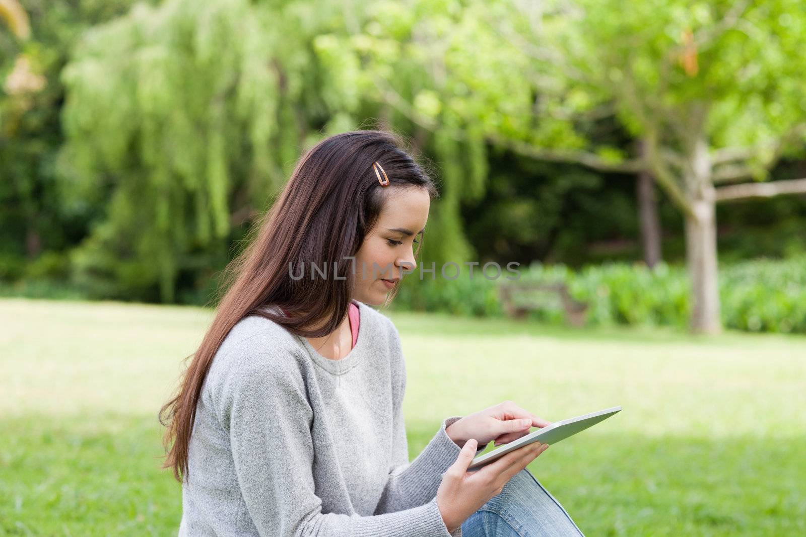 Young relaxed woman sitting in a public garden while using her tablet computer
