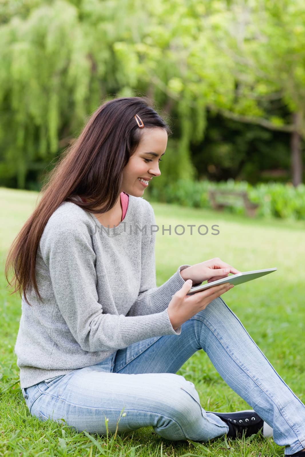 Smiling young girl using her tablet computer while sitting in the countryside