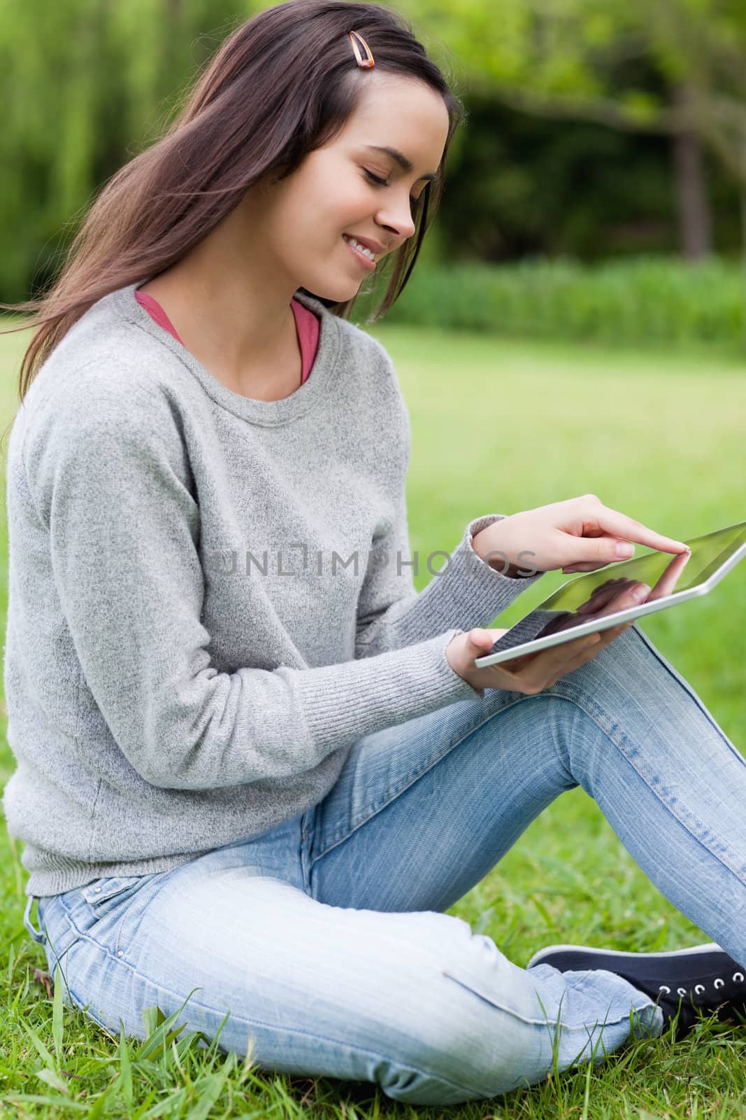 Young smiling woman sitting on the grass in a park while using h by Wavebreakmedia