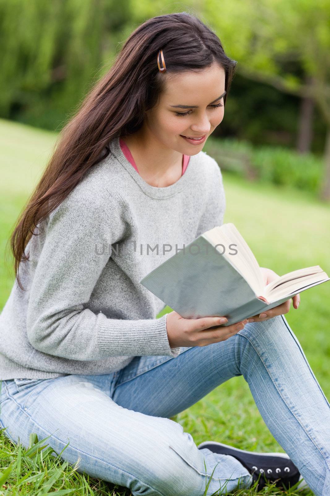 Young relaxed girl sitting on the grass in a park while reading  by Wavebreakmedia