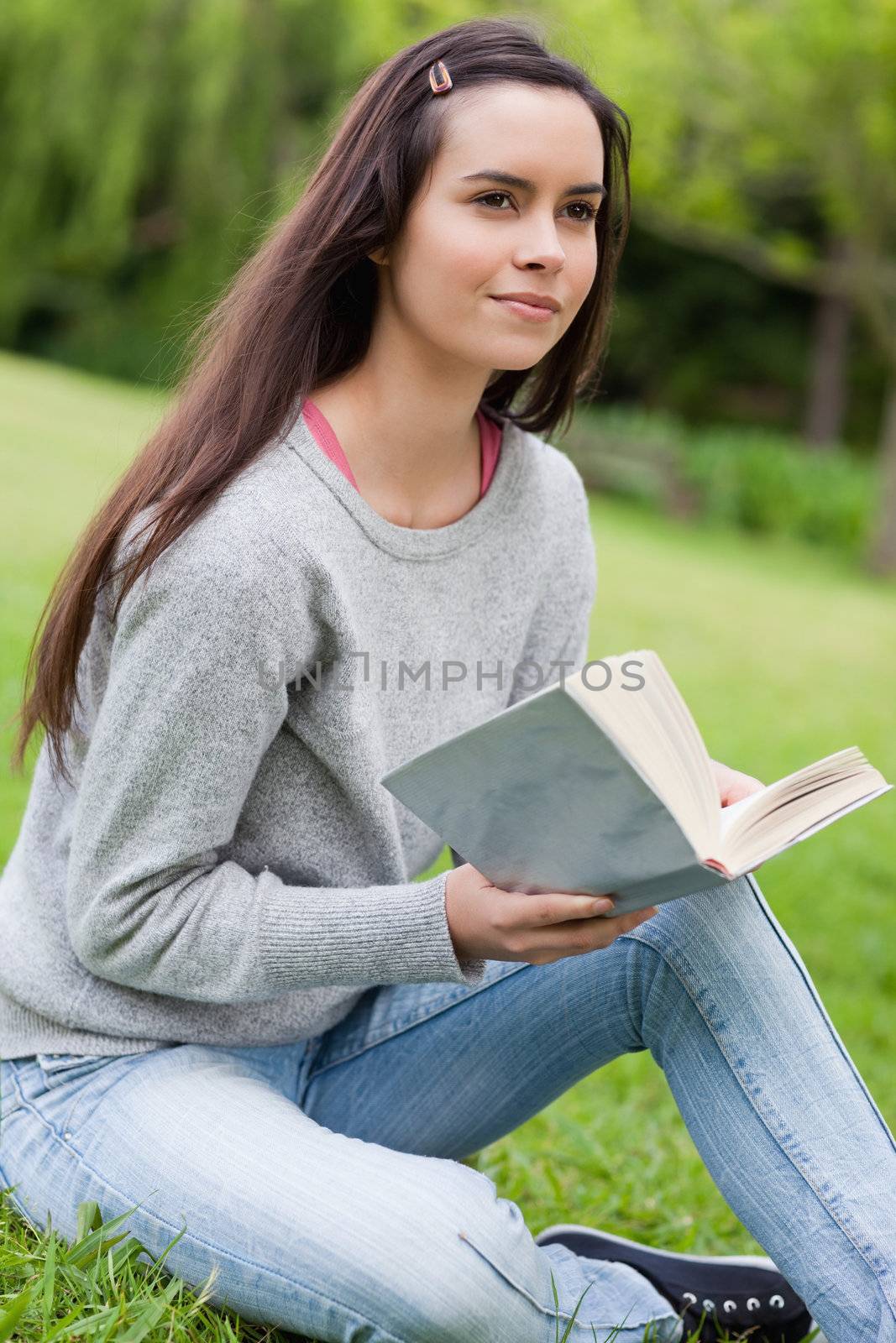 Thoughtful young girl holding a book while sitting on the grass in the countryside