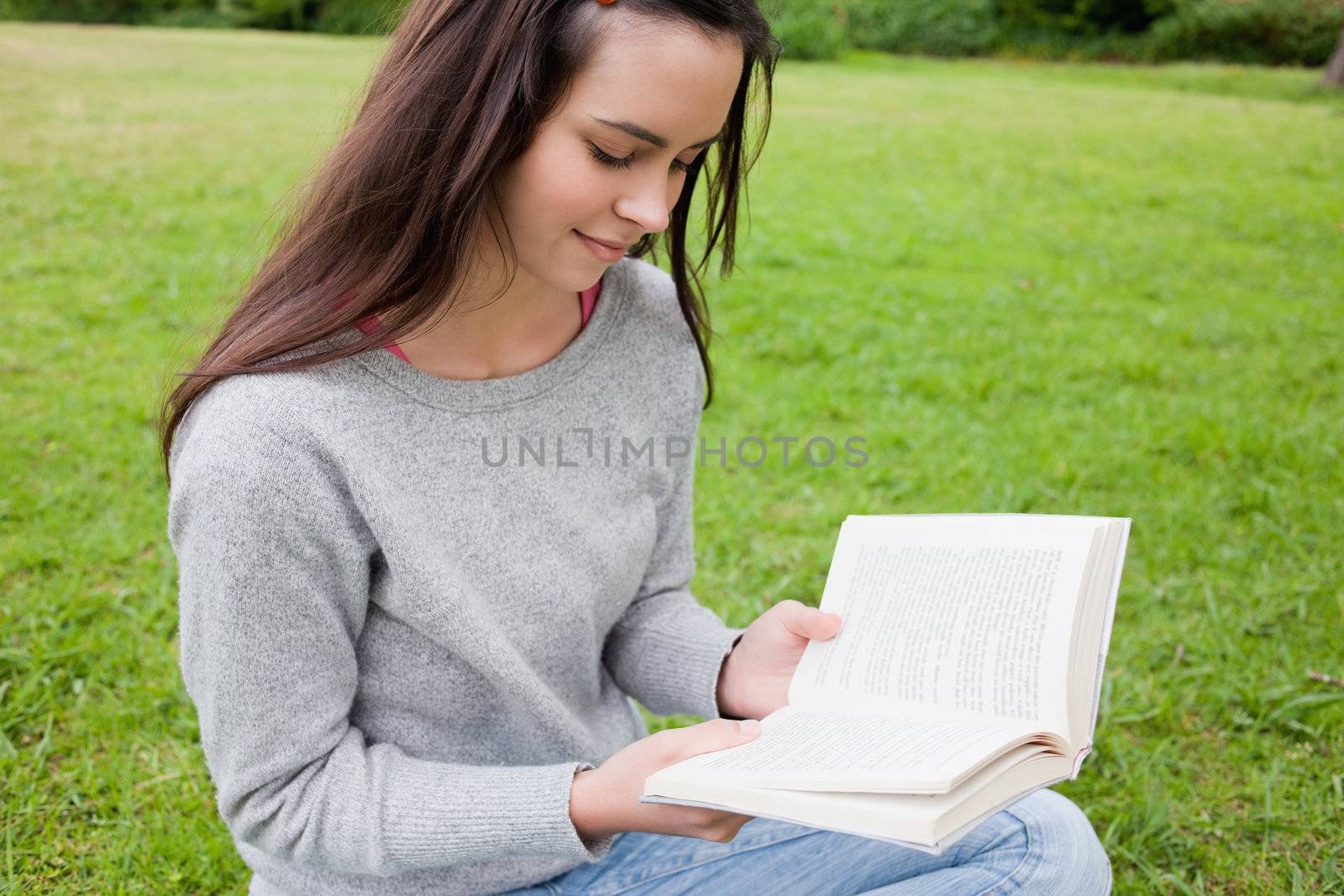 Young relaxed girl attentively reading a book while sitting down in a parkland