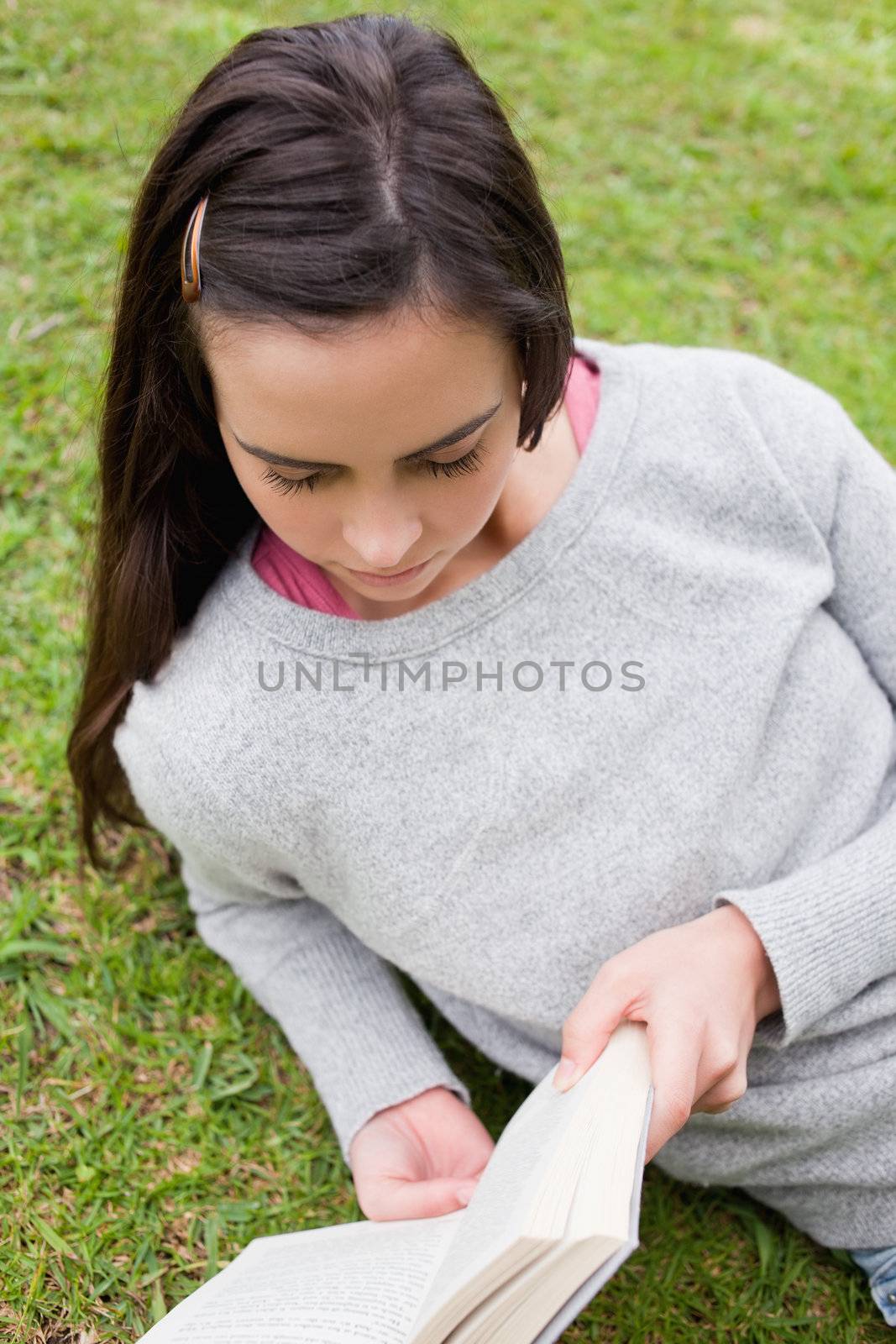 Young serious woman reading a book while lying on the side in the countryside