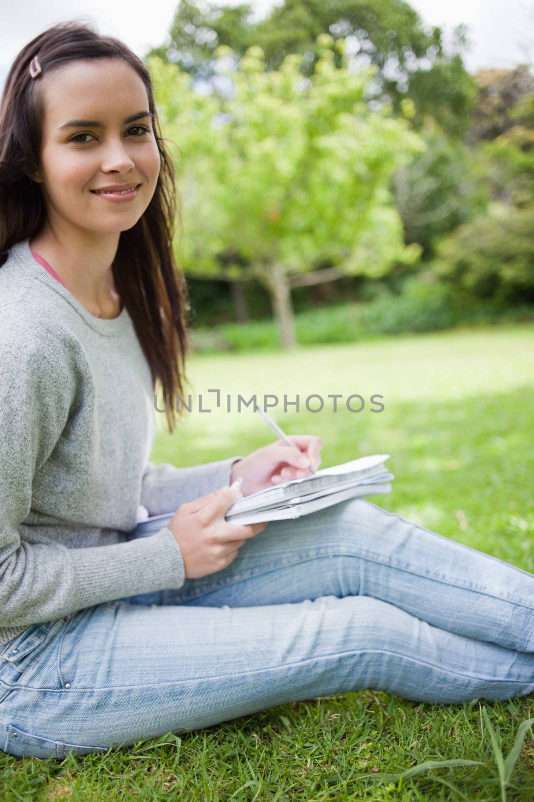 Young happy student sitting in a public garden while doing her homework