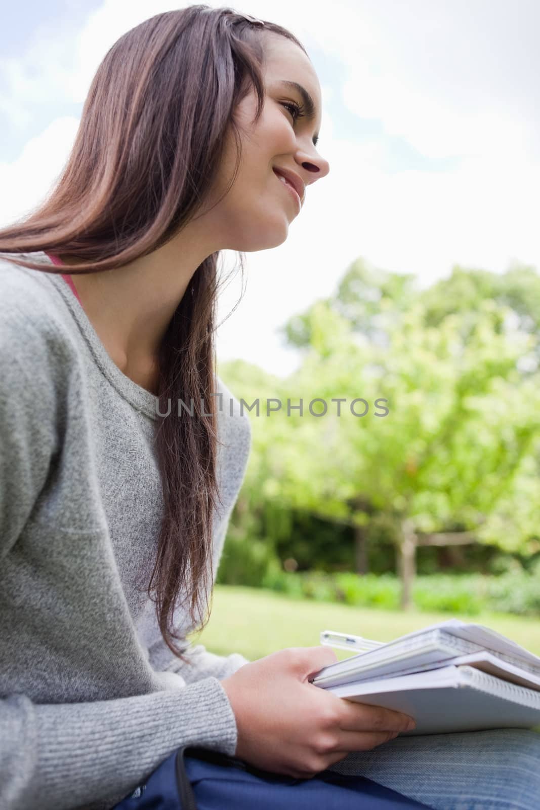 Smiling young student doing her homework while sitting down in the countryside