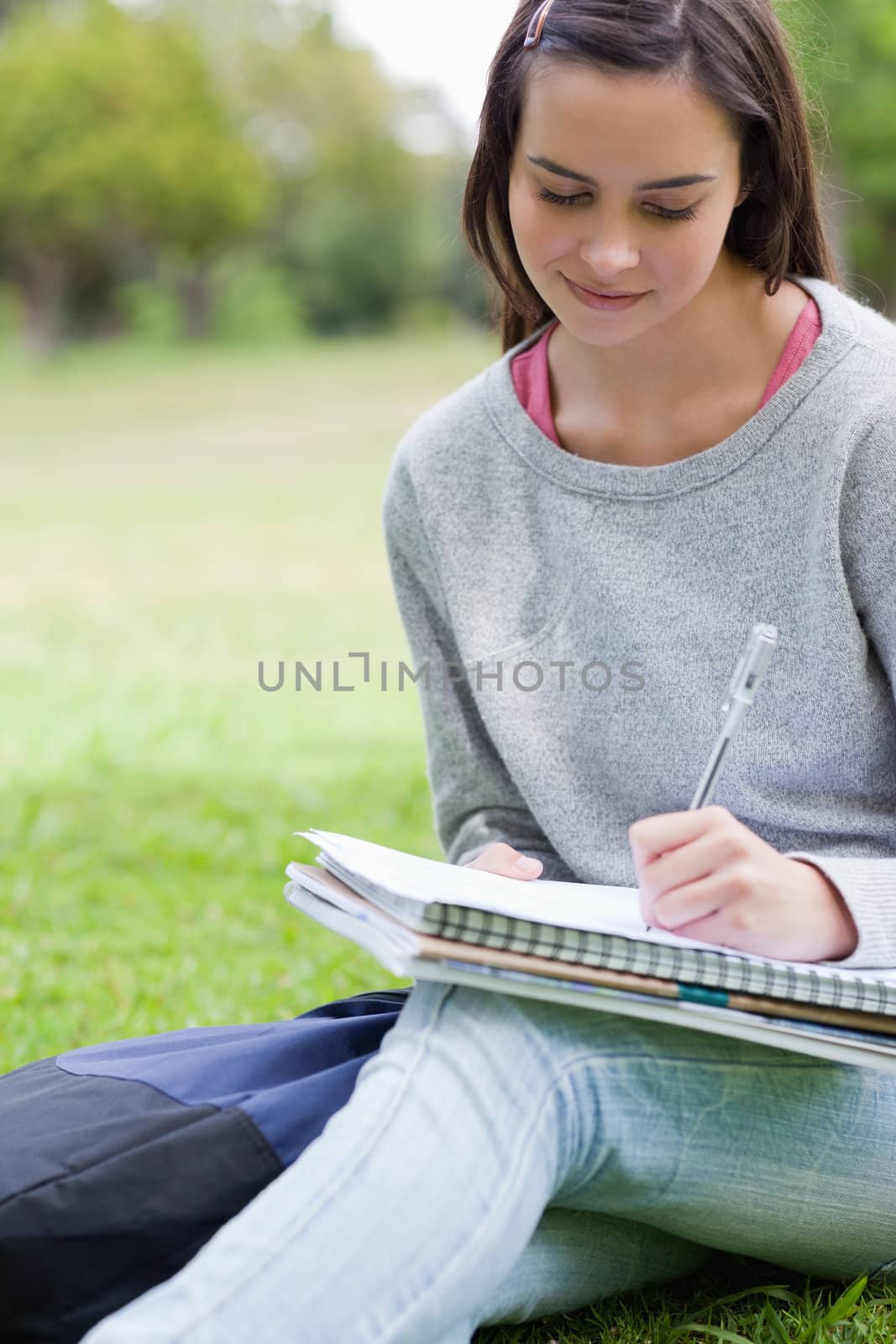 Young smiling student writing on her notebook while sitting down in the countryside