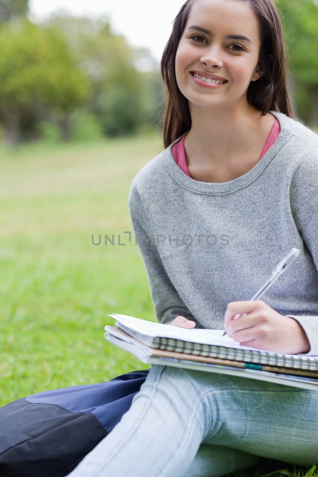 Smiling student doing her homework while sitting down in the countryside
