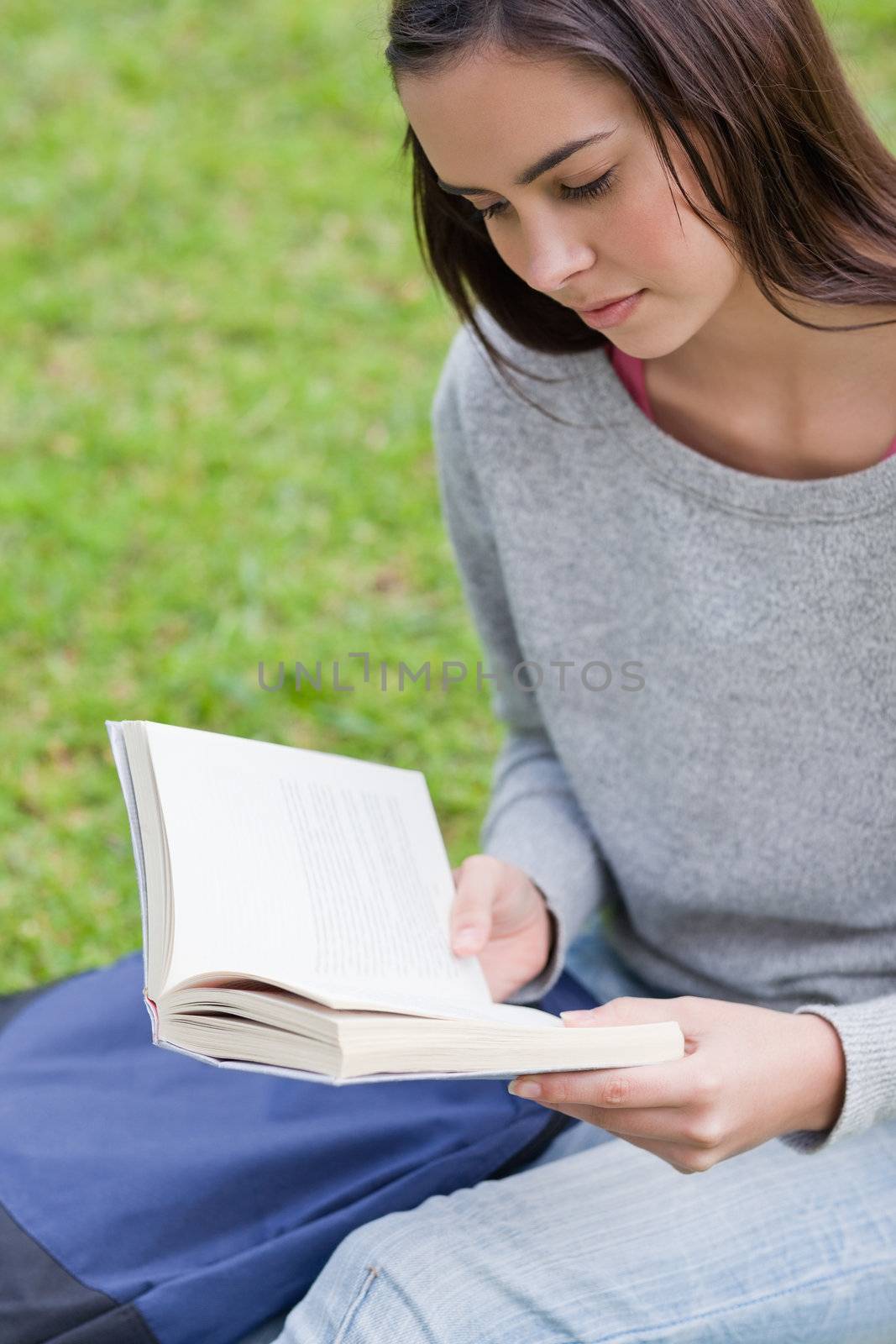Serious young woman sitting on the grass in a public garden while reading a book