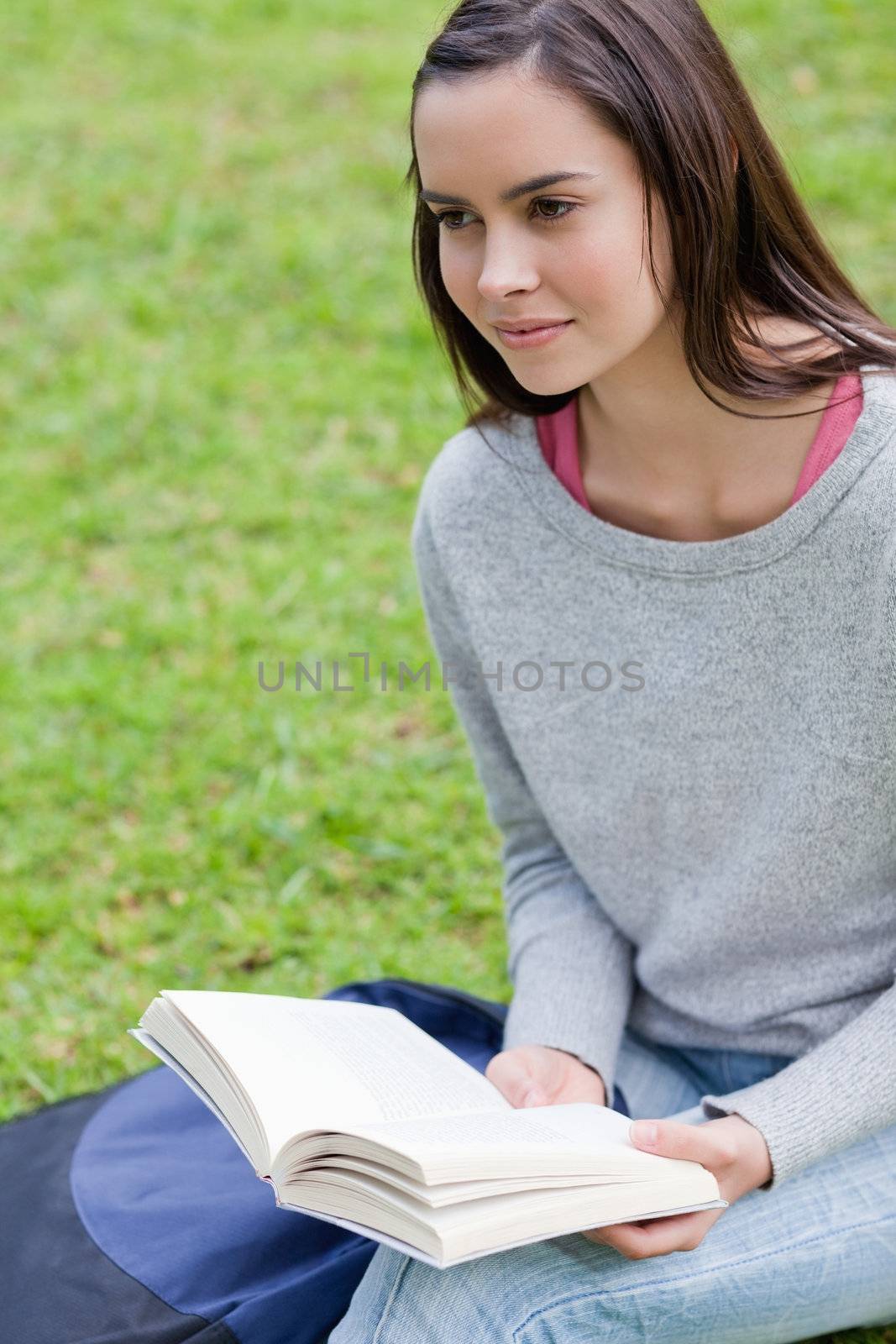 Young calm woman reading a book in a park while looking towards  by Wavebreakmedia