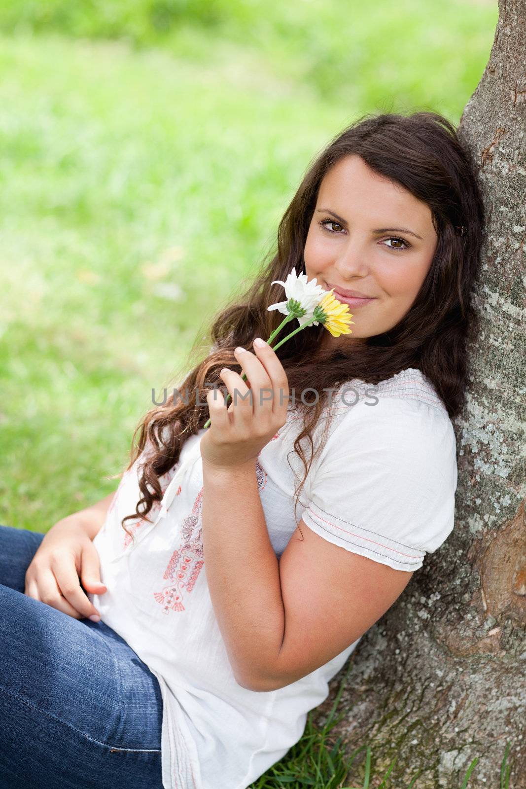 Young smiling woman smelling flowers while sitting against a tre by Wavebreakmedia