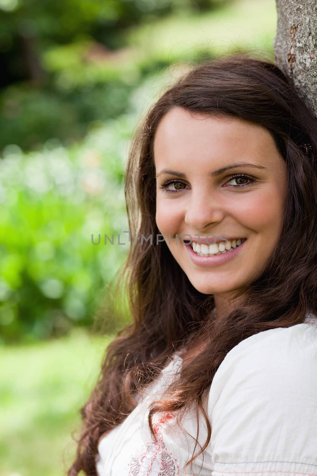 Young woman leaning against a tree in the countryside while showing a great smile