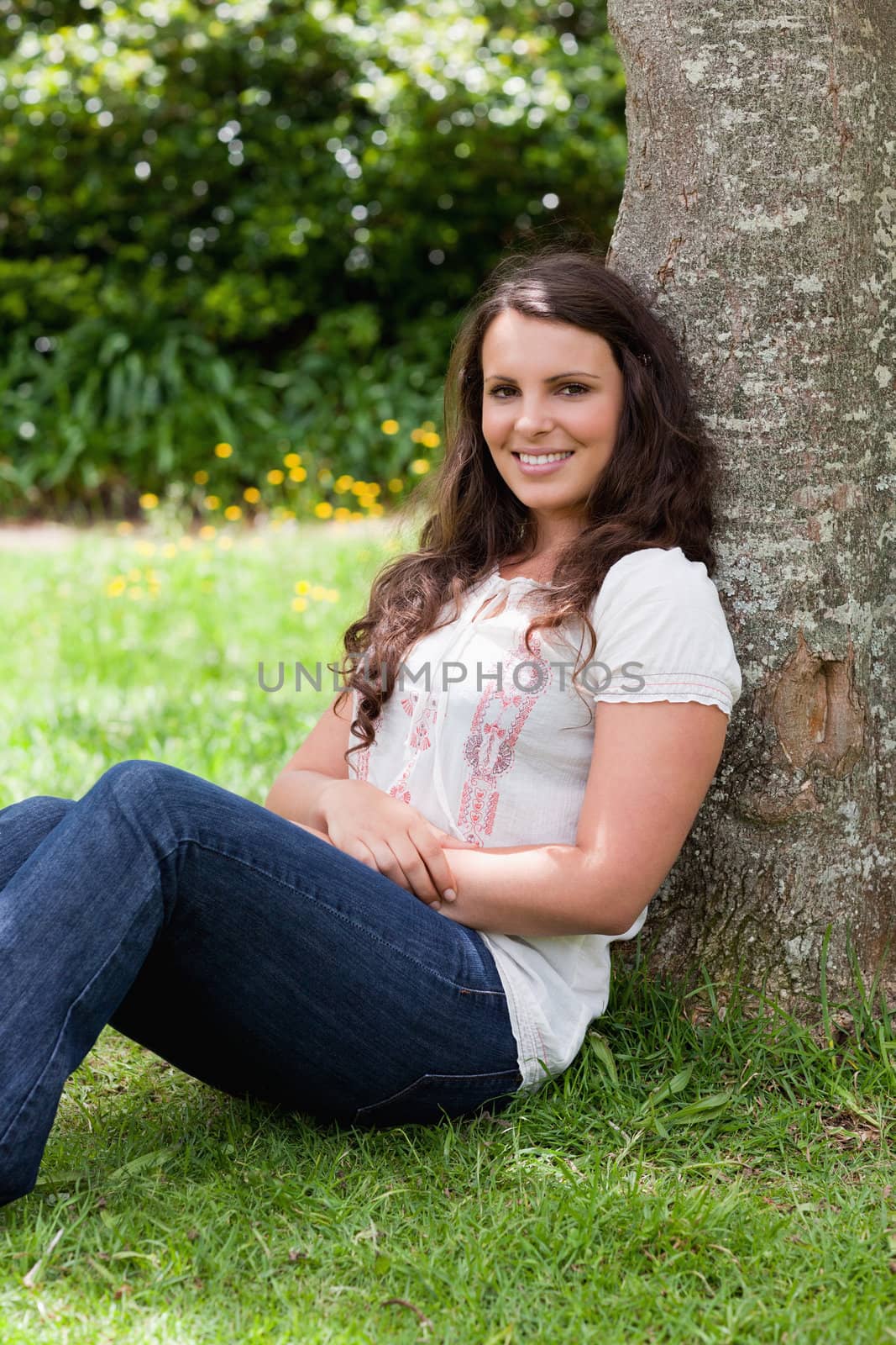Young smiling woman sitting against a tree with arms crossed by Wavebreakmedia