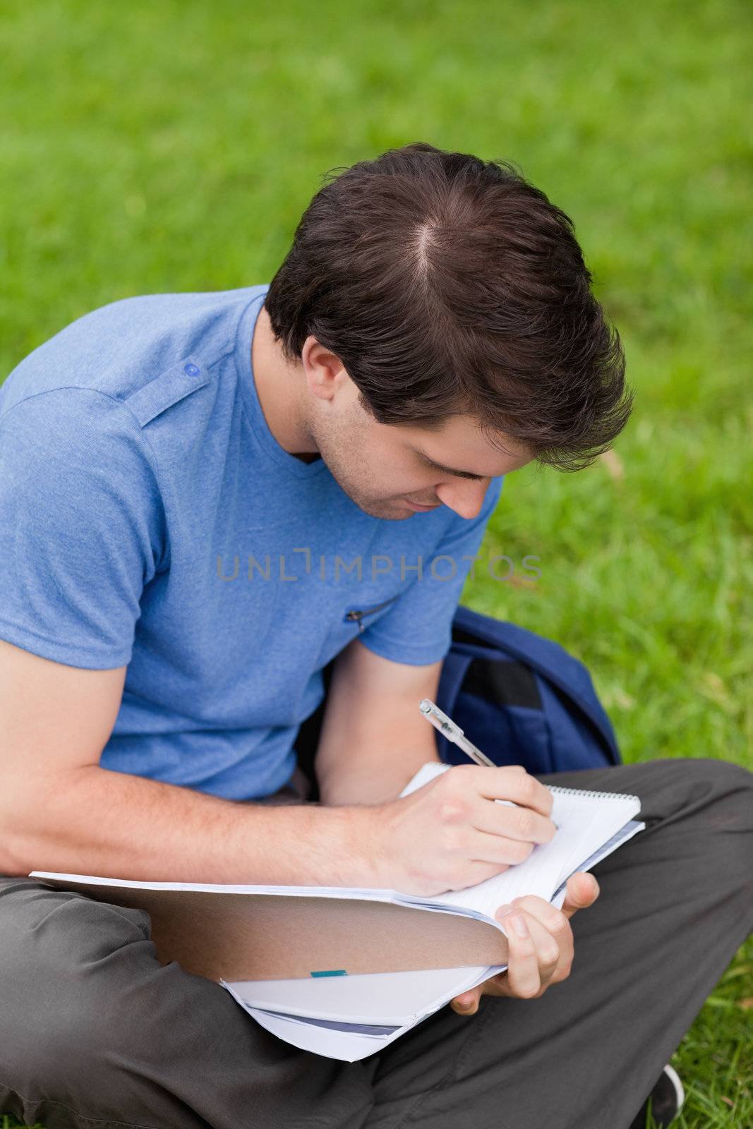 Young student sitting on the grass while writing on his notebook by Wavebreakmedia