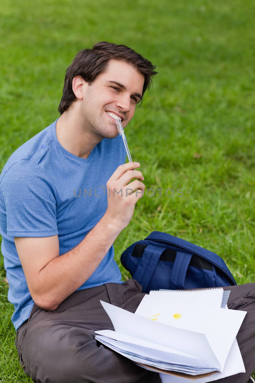 Young smiling man working while sitting on the grass in the countryside