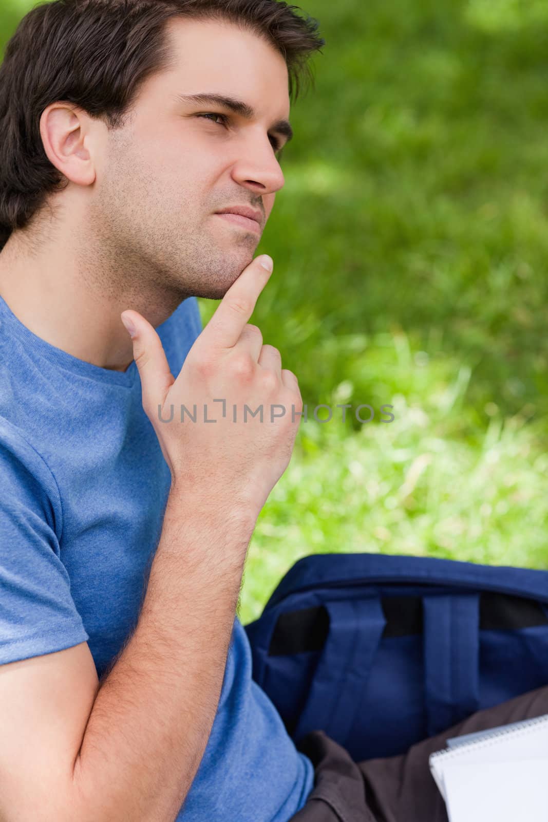Young thoughtful man placing his finger on his chin while sitting in the countryside