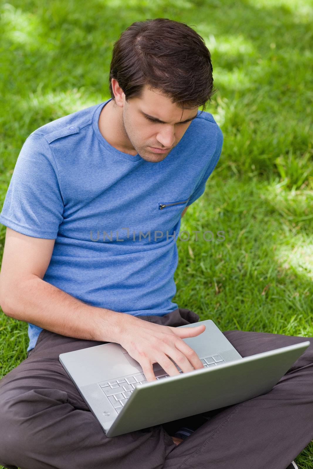 Young serious man working on his laptop while sitting in a park by Wavebreakmedia