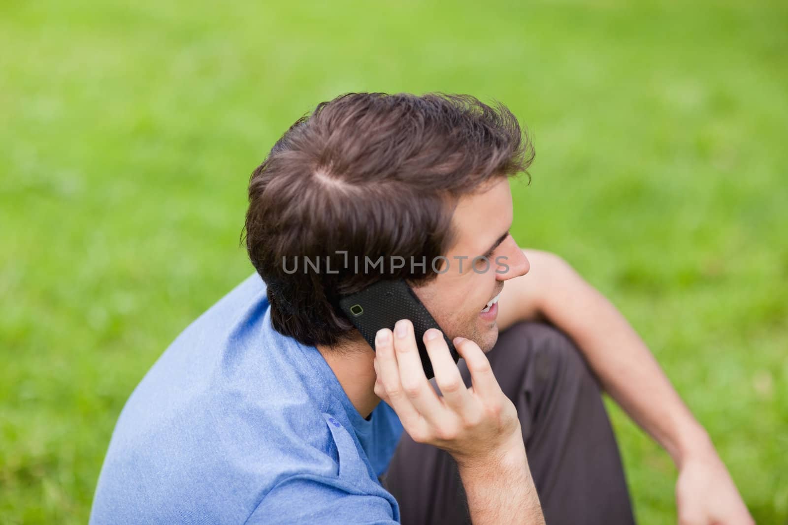 Young smiling man talking on the phone while sitting in a park by Wavebreakmedia