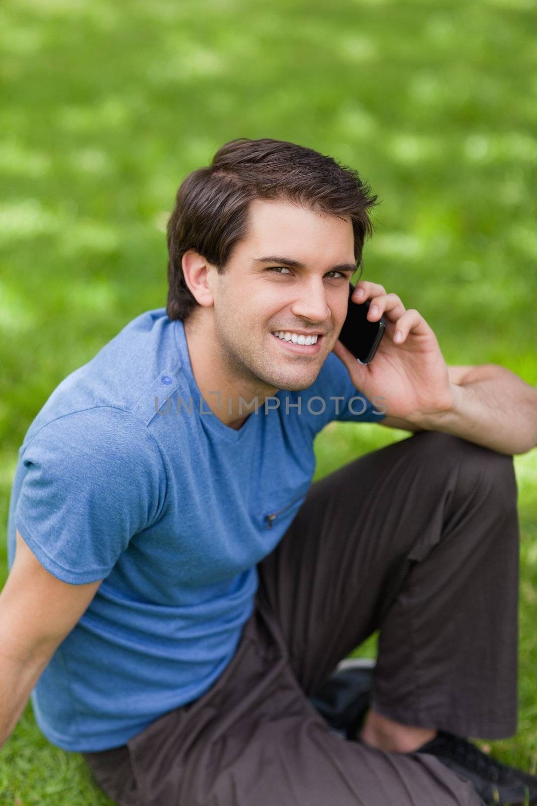 Young happy man talking with his mobile phone while sitting in a public garden