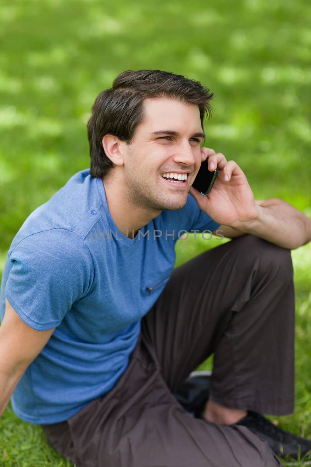 Young happy man laughing while sitting in the countryside and talking on the phone