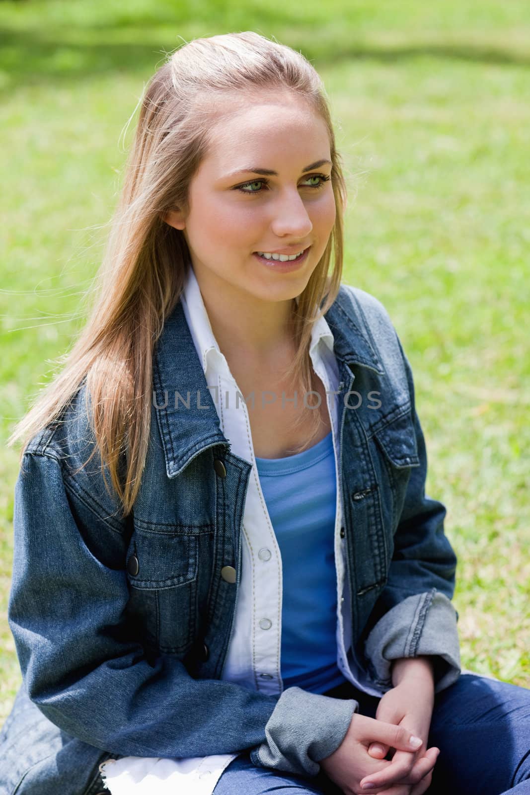 Young smiling girl sitting on the grass in a park while crossing her hands