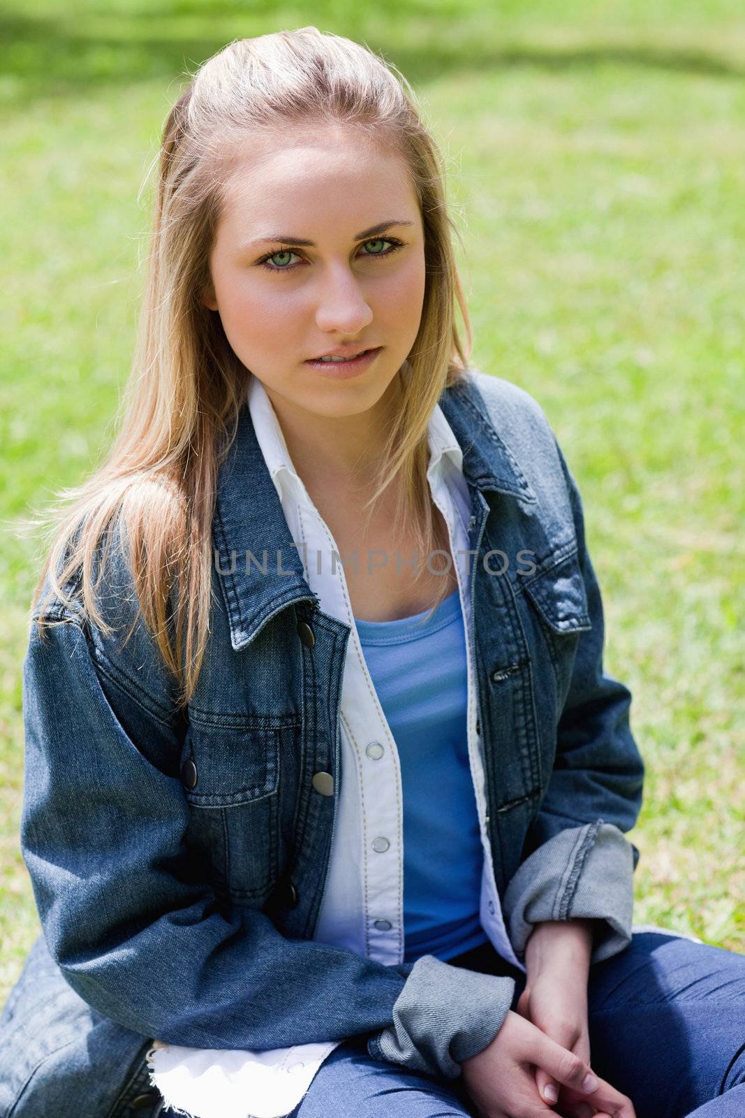 Young serious girl sitting on the grass in the countryside while looking at the camera