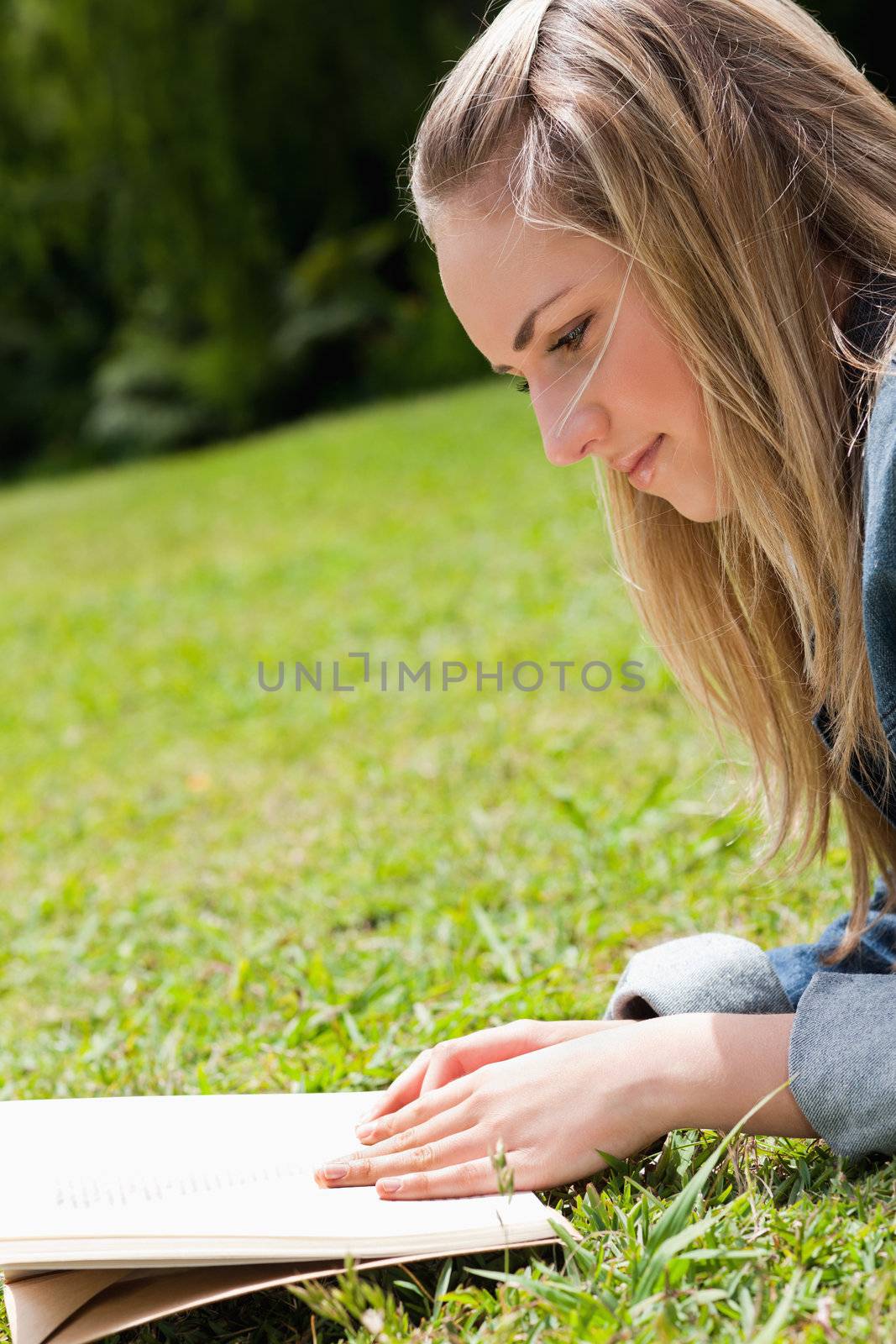 Young blonde girl lying on the grass while reading a book by Wavebreakmedia