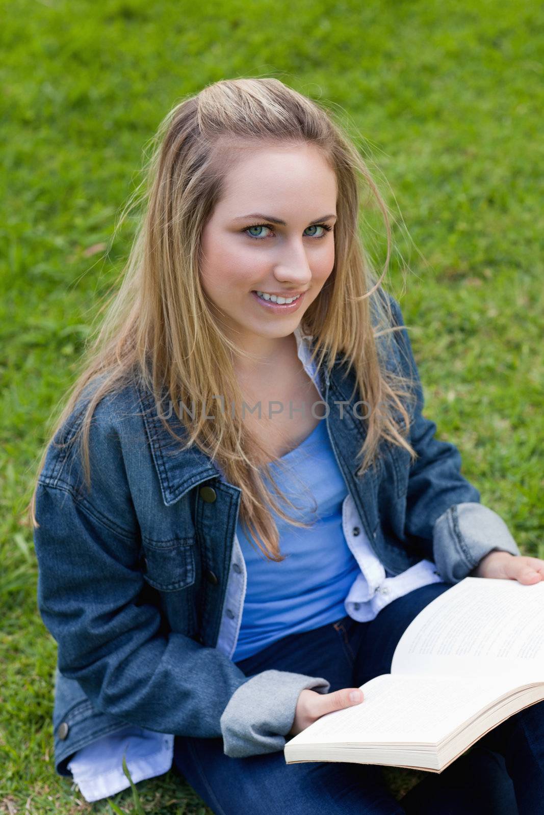 Young woman looking at the camera while holding a book and sitting on the grass