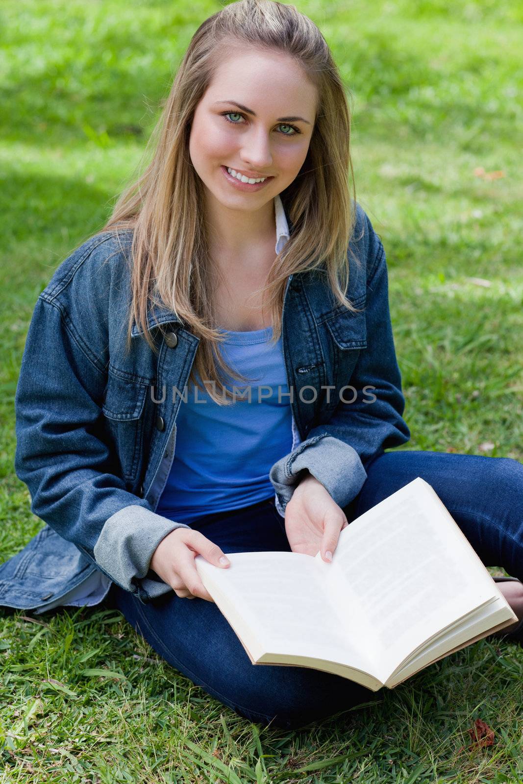 Young blonde girl sitting cross-legged on the grass while holding a book