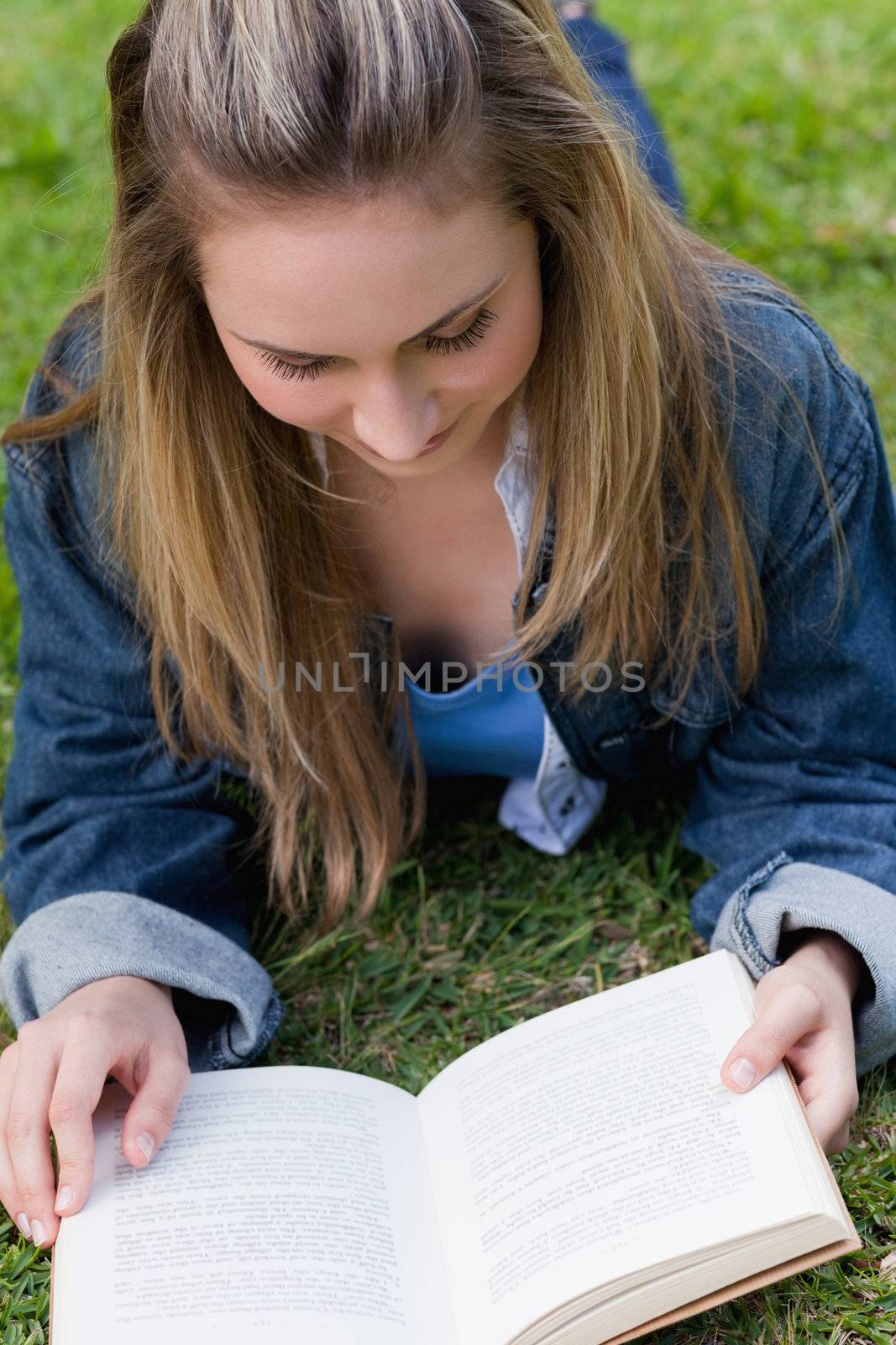 Young relaxed girl lying on the grass while reading a book by Wavebreakmedia