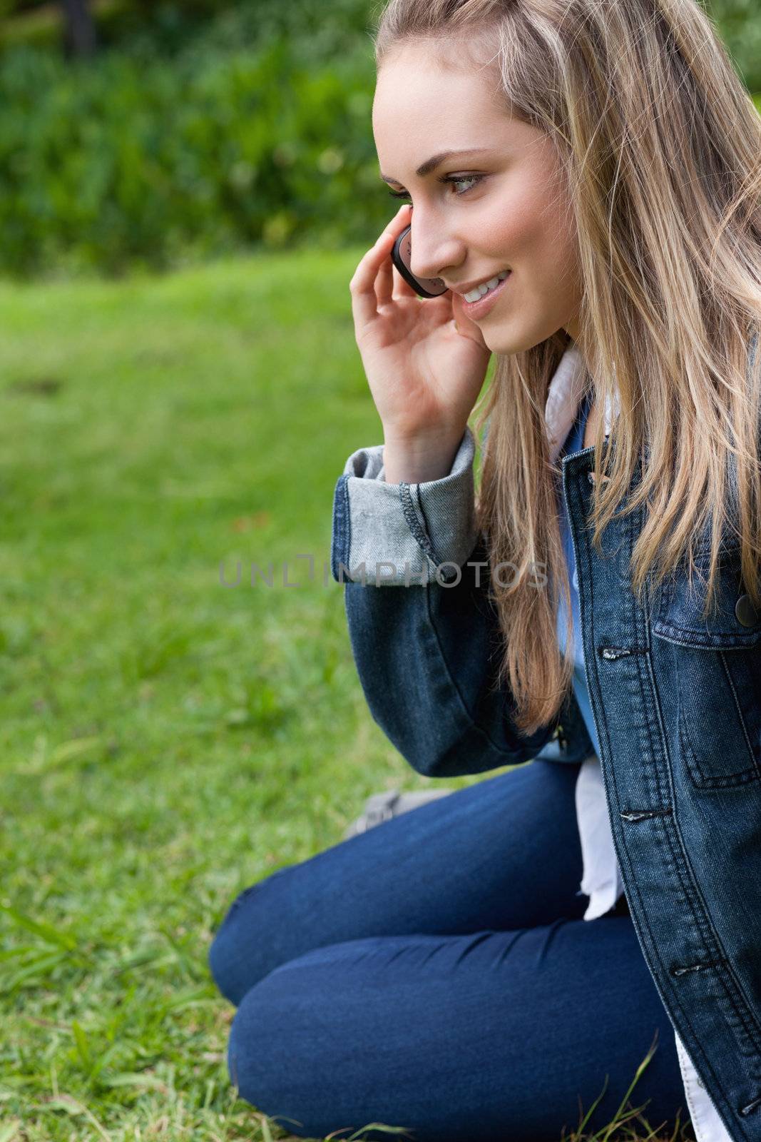 Young smiling girl talking on the phone while sitting on the grass in the countryside
