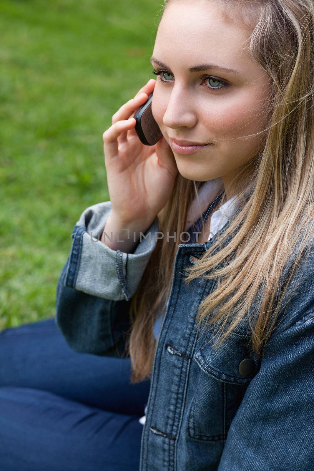 Young blonde woman calling with her cellphone while sitting down in a public garden
