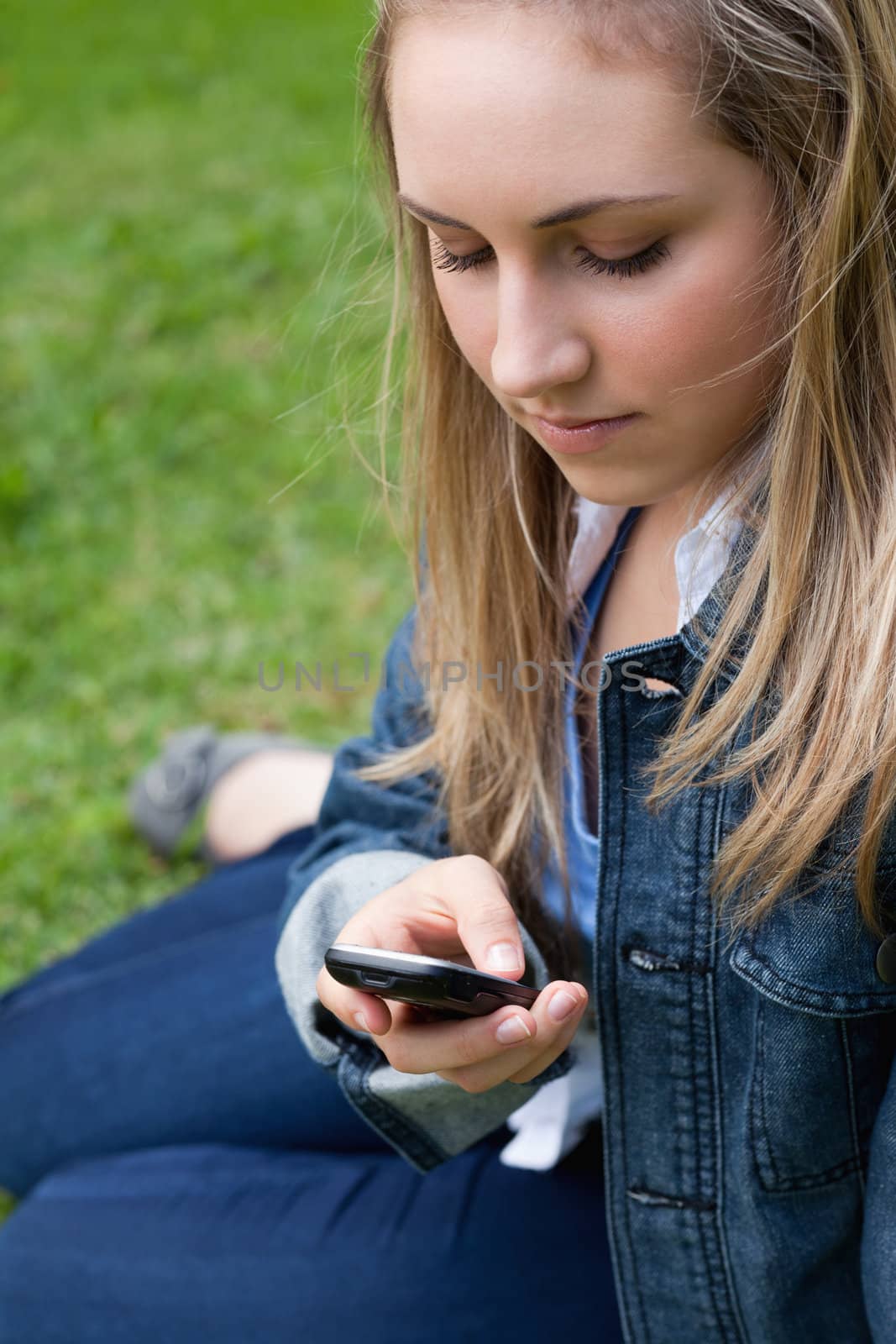 Young girl sending a text while sitting on the grass by Wavebreakmedia