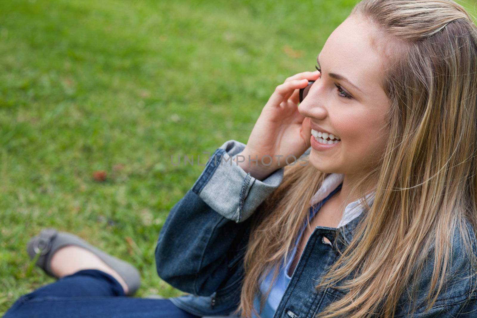 Young happy blonde girl calling with her mobile phone while sitting in the countryside