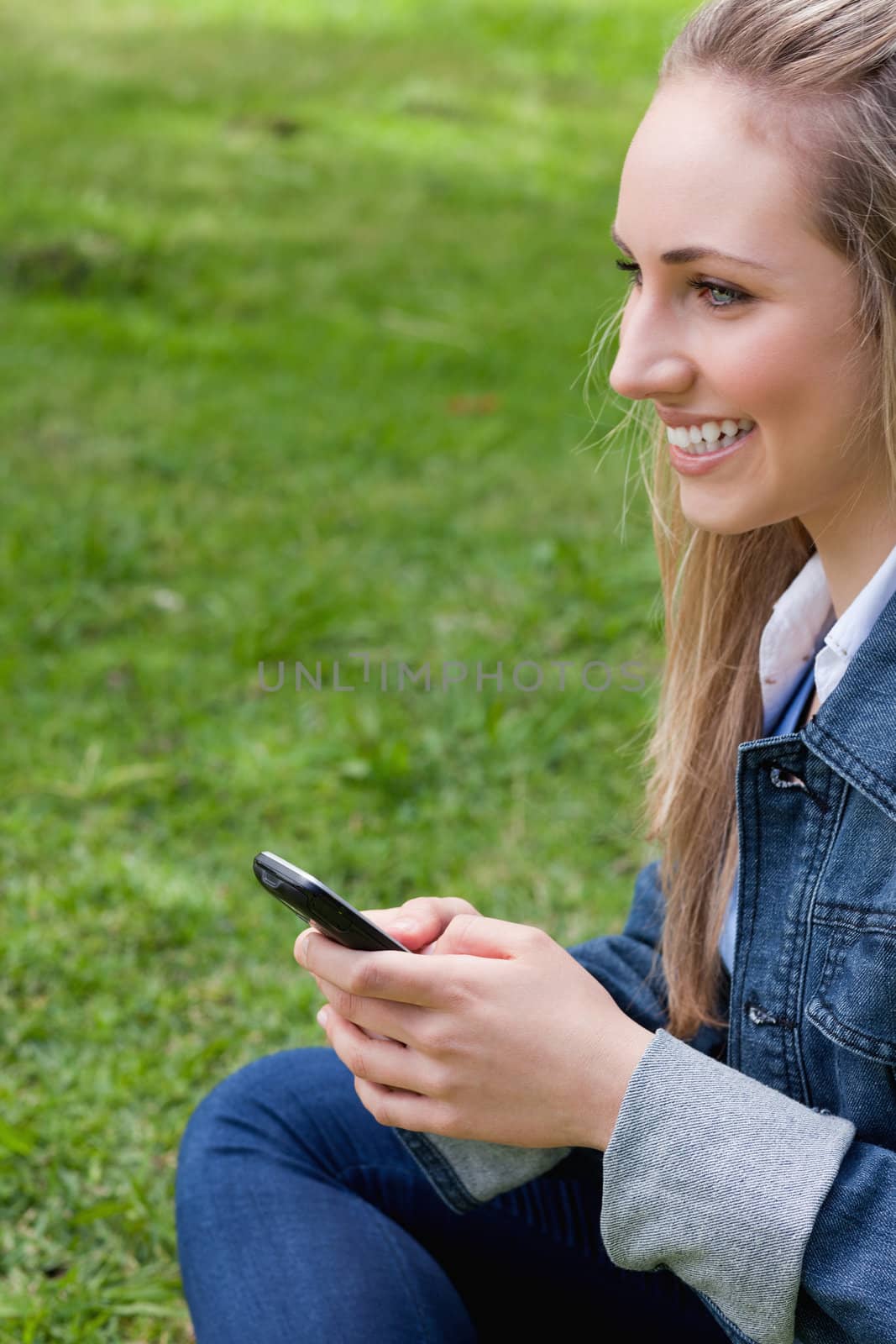 Young smiling woman sending a text while looking away and sitting in a parkland