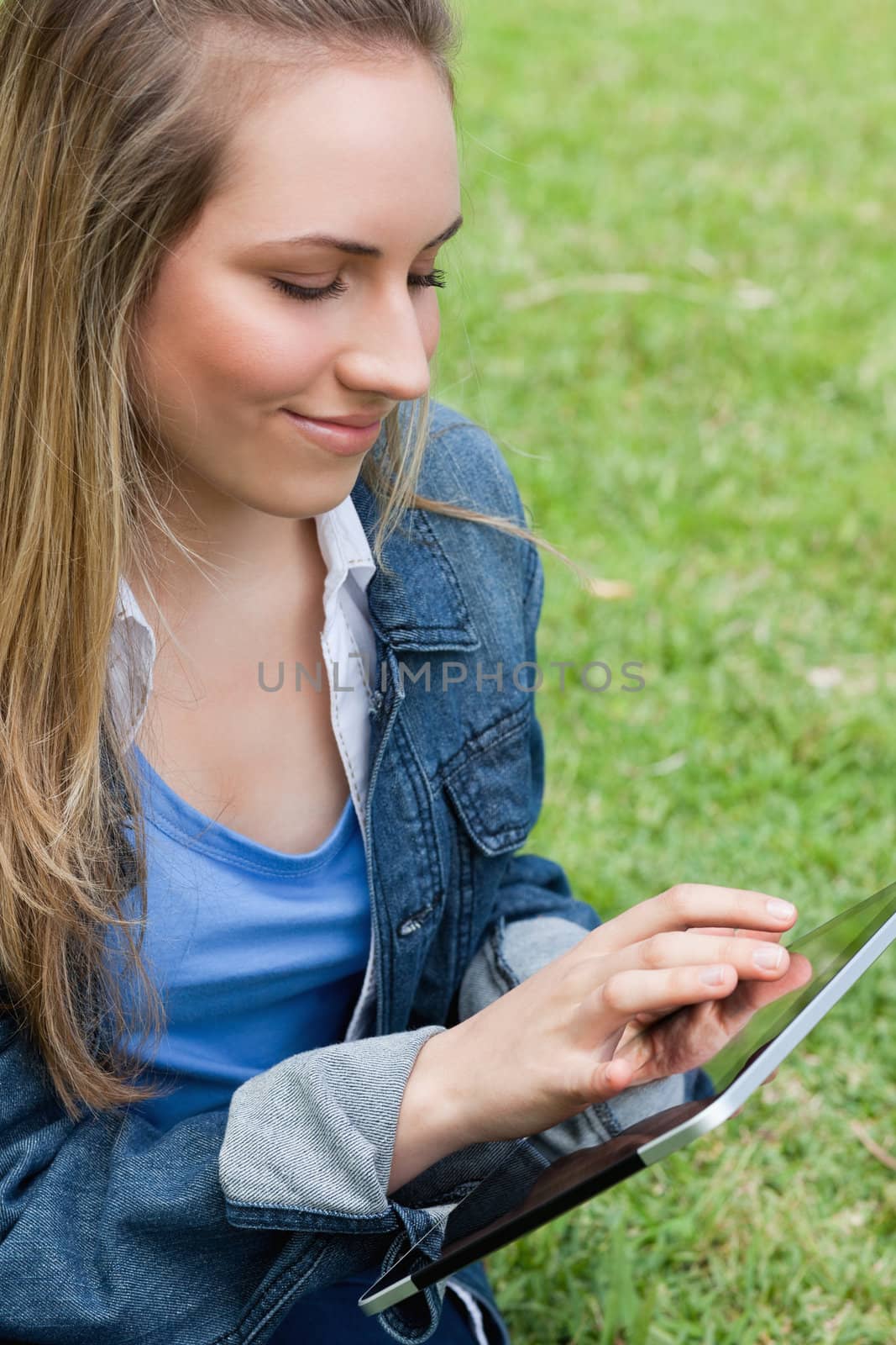 Young peaceful woman using her tablet pc while sitting on the gr by Wavebreakmedia