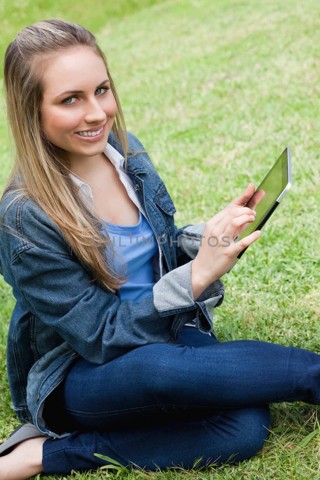Young happy girl looking at the camera while touching her tablet pc in a parkland