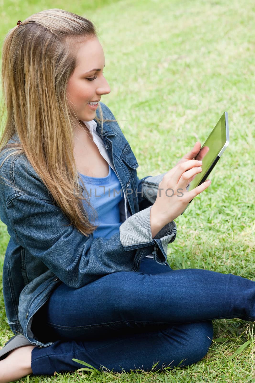 Young attractive blonde girl sitting in a park while touching her tablet computer