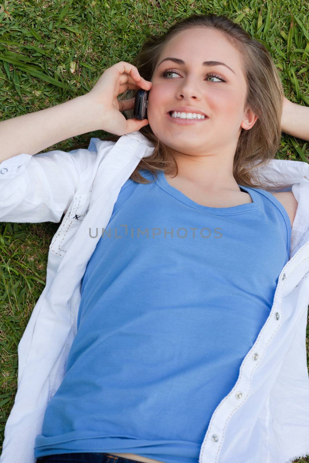 Young smiling girl lying on her back on the grass while using her mobile phone