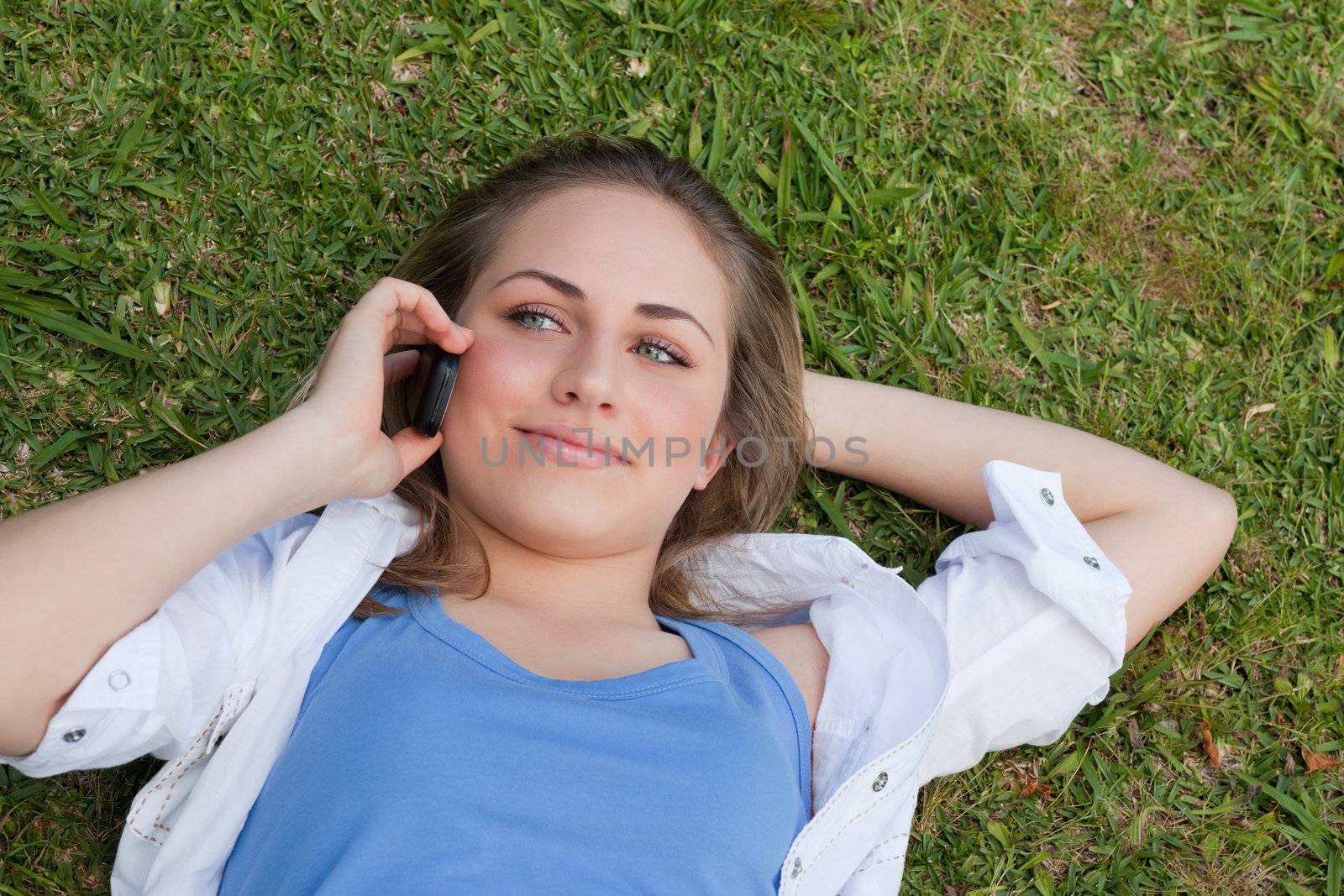 Young relaxed blonde girl lying on her back while using her mobile phone