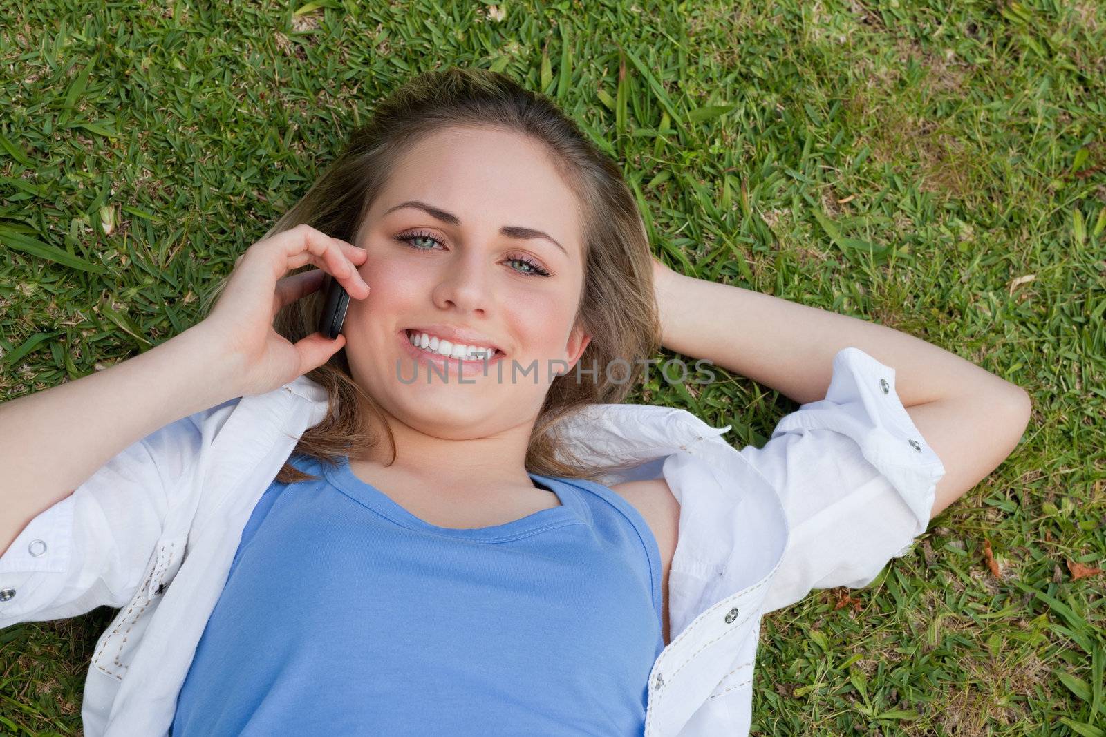 Young smiling blonde girl lying on her back in a parkland while looking up