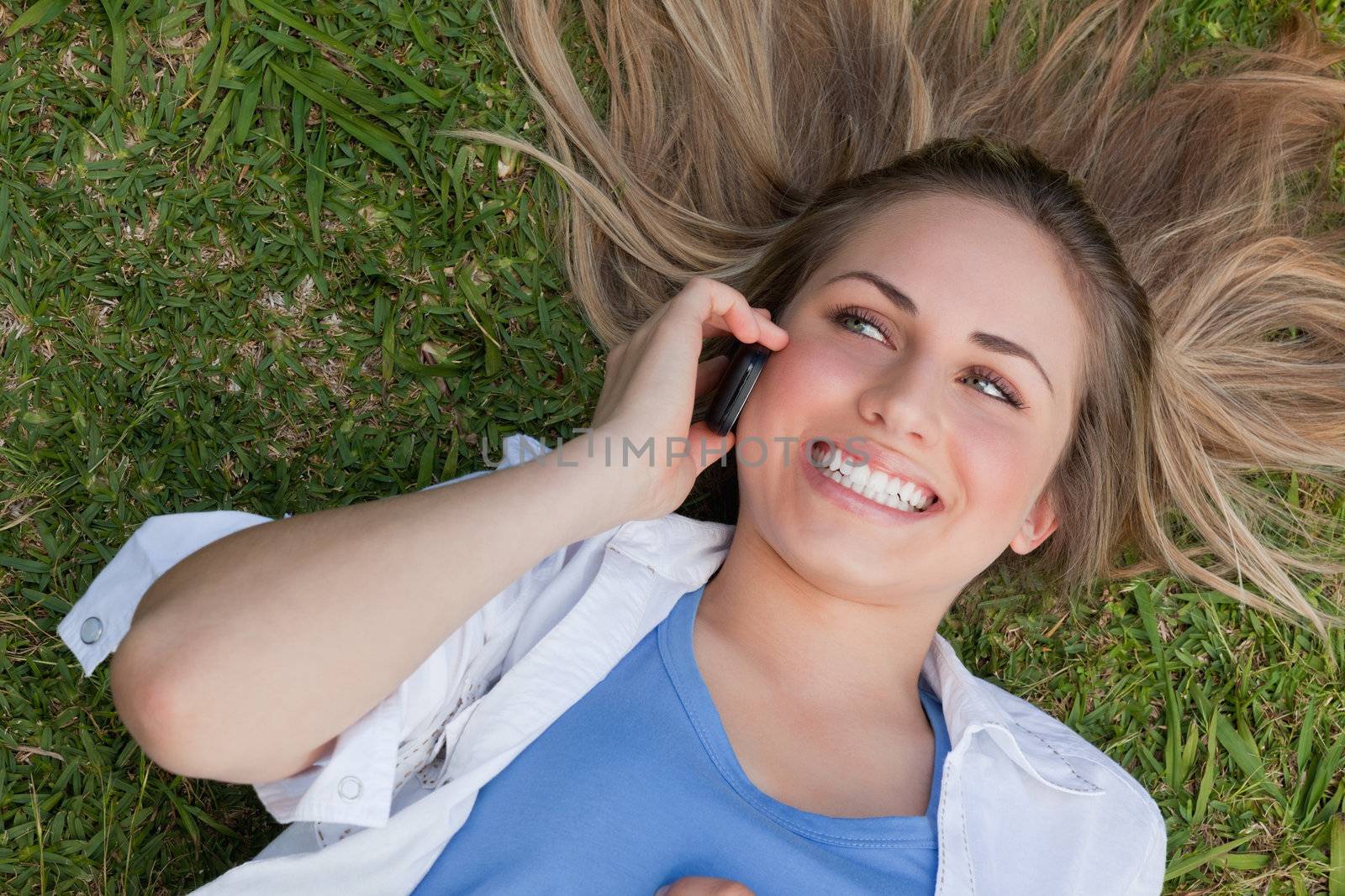 Young smiling woman lying on her back while using her cellphone by Wavebreakmedia