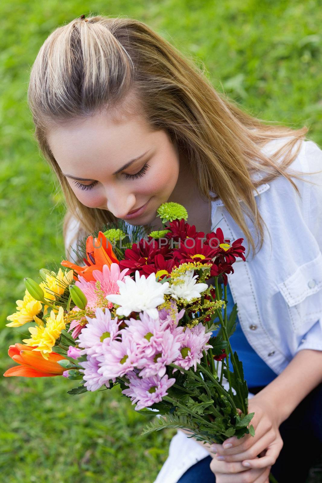 Young attractive girl smelling a bunch of flower while sitting on the grass