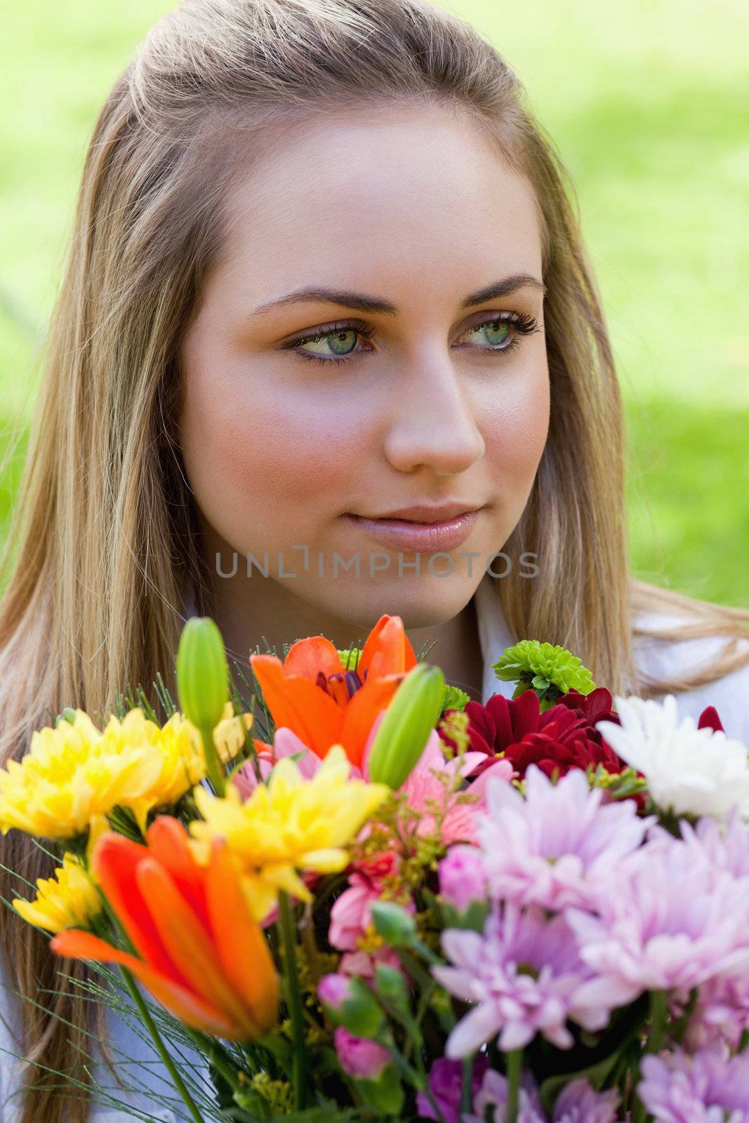 Young blonde girl holding a bunch of flowers while looking away in the countryside