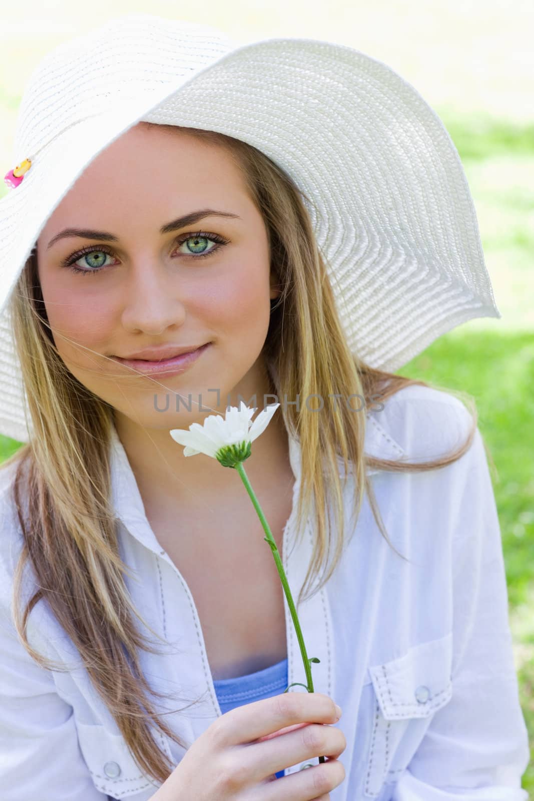 Young blonde girl wearing a hat while holding a beautiful white flower in a parkland