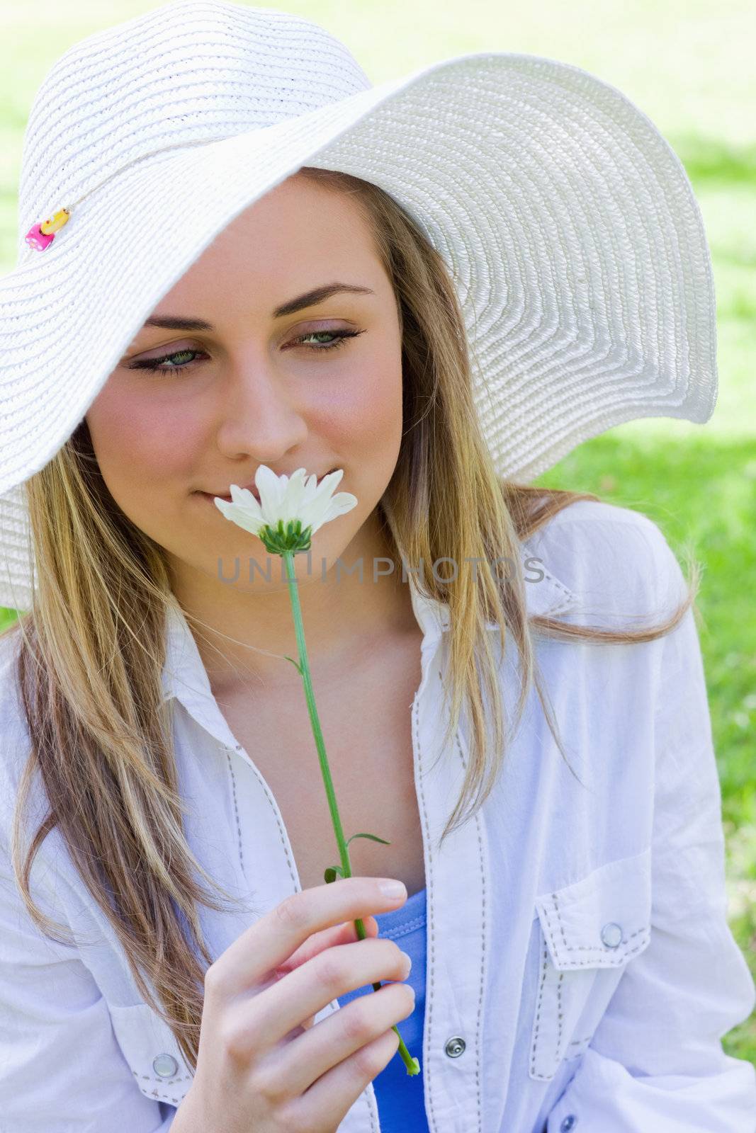 Young peaceful blonde girl smelling a beautiful white flower while looking down