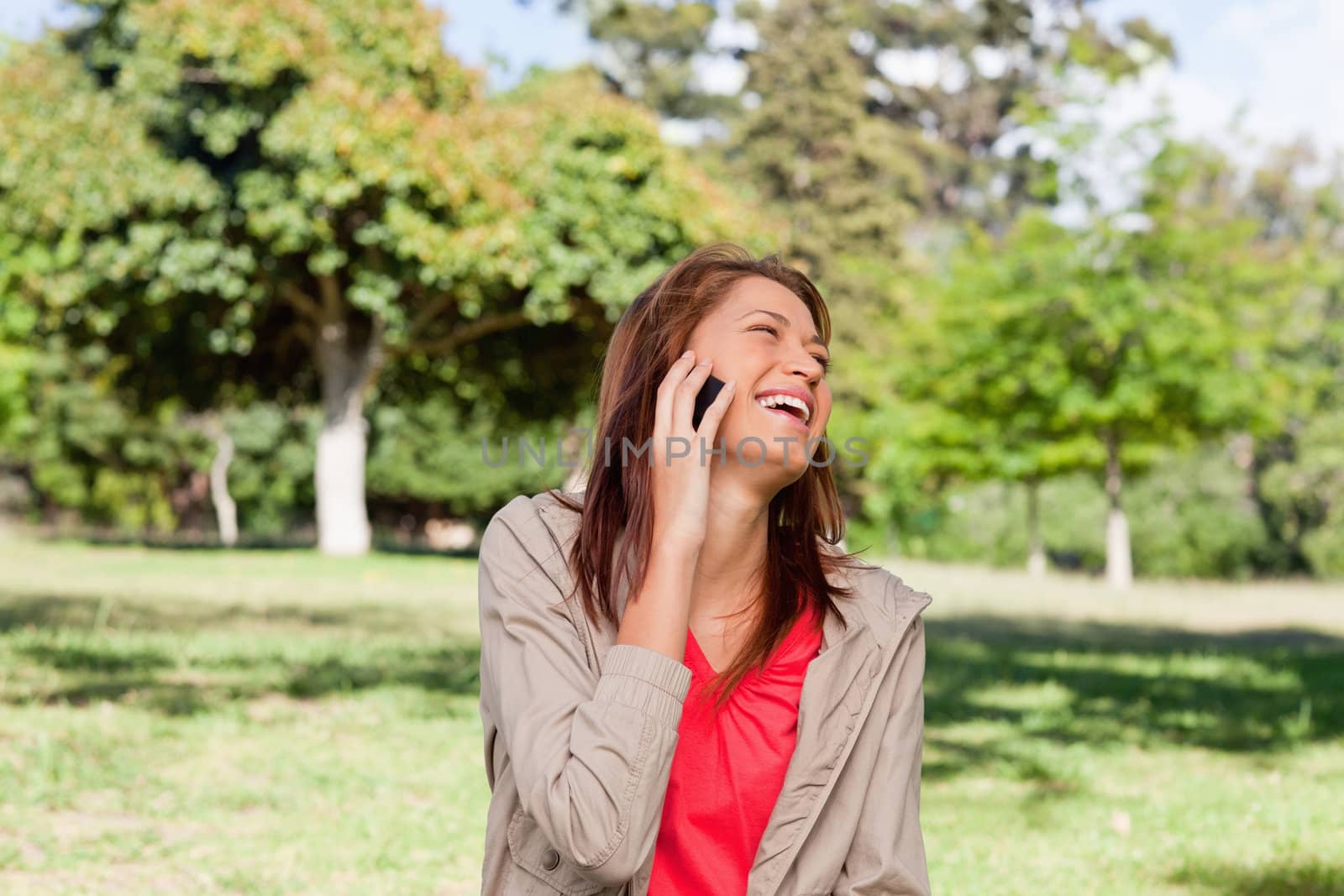 Woman laughing happily on a phone while standing in a bright grassland environment