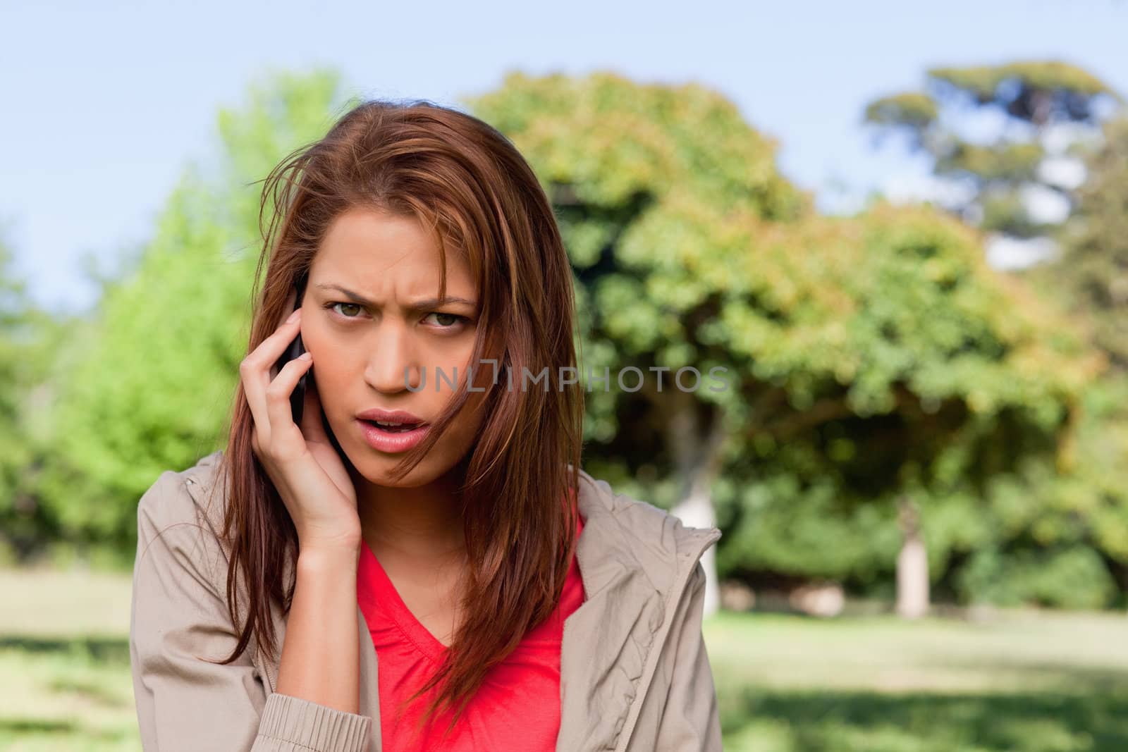 Woman with a serious expression talking on the phone in a bright by Wavebreakmedia