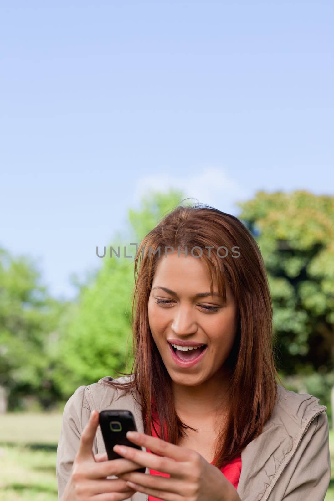 Woman joyfully reading a text message in a bright area surrounded by trees